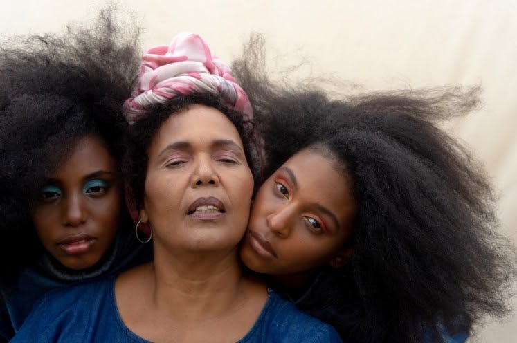 Portrait of black sisters leaning on aunt's shoulder