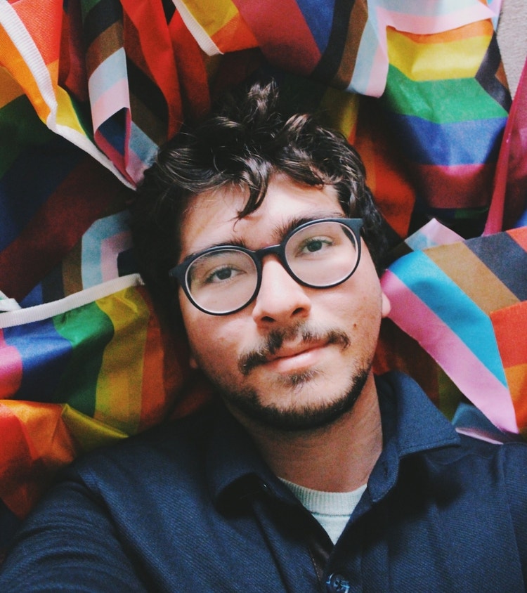 A selfportrait where I'm laying with a bunch rainbow & progress pride flags and feeling cosy about it, comfortable with the person I've grown into. 