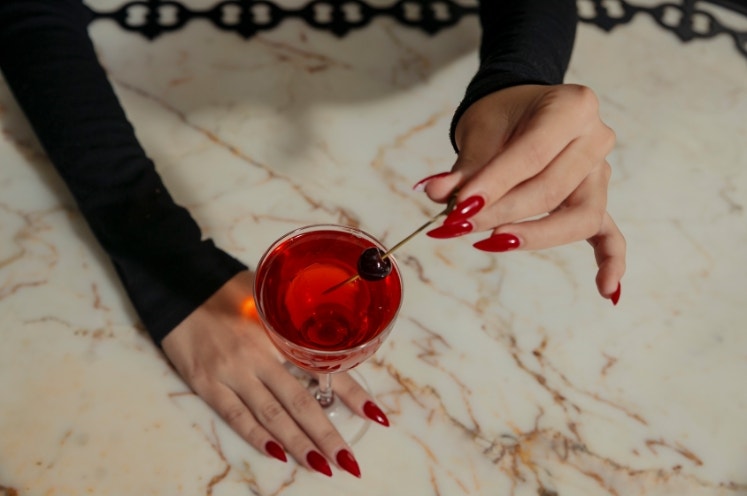 A person holding a cocktail with long red nails at a bar