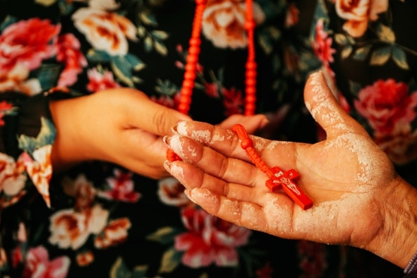 Cropped image of mature woman's hand with dough holding red cross pendant worn by young female friend