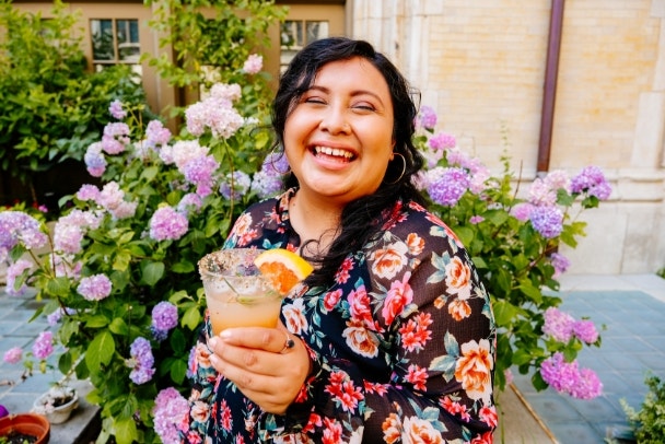 Portrait of young woman laughing while holding cocktail glass with orange slice at backyard during garden party