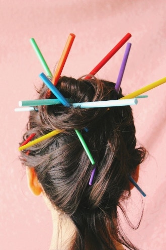 womans long hair wrapped with colorful chopsticks and pink background