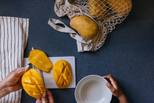 Asian grandmother cutting mango snack for grandchild