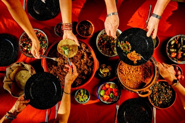 Overhead shot of a dinner table with Mexican food and hands. Tacos, beans, carnitas, habanero, salsa