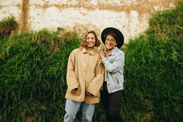 Amigos jóvenes bisexual y queer abrazados frente a una pared con vegetación