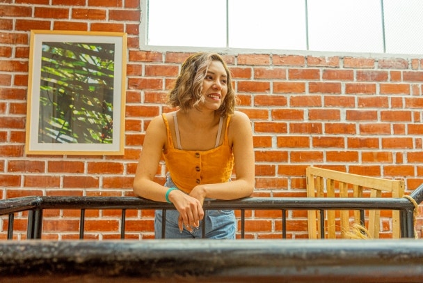 Joven bisexual sonriendo hacia un lado frente a una pared de ladrillos