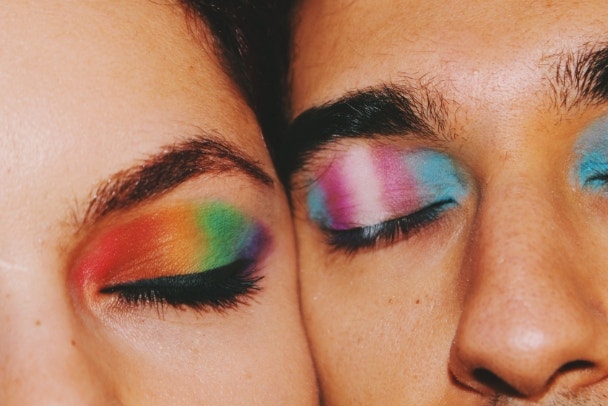 Closeup portrait of queer friends / young couple faces & eyes wearing eyeshadow makeup of lgbtq rainbow pride flag & trans pride flag