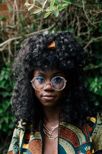 Portrait of woman with curly hair and glasses wearing African print jacket in nature