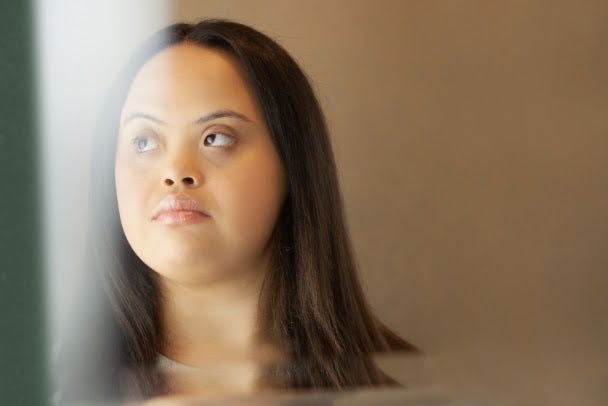 Young biracial woman with Down Syndrome looking into the mirror in the bathroom