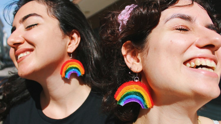 two women friends smiling with glasses wearing rainbow pride flag themed earrings