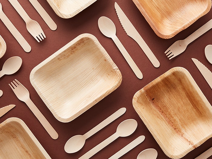 Flatlay composition from above. Biodegradeable cutlery and food containers on brown table.