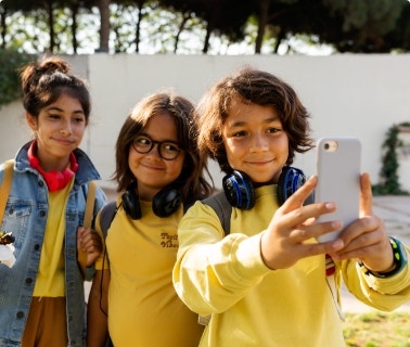 Three elementary-aged children in bright clothes take selfie outside at school.