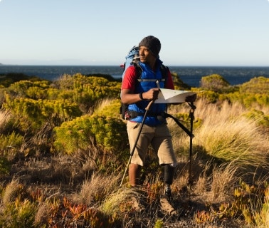 Man with hiking gear, prosethetic leg stands outdoor in grasses and sun.