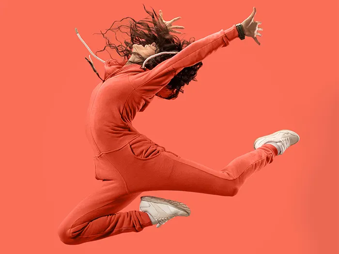 Freedom in moving. Mid-air shot of pretty happy young woman jumping and gesturing against coral studio background.