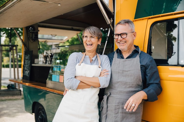 Happy mature couple looking away while standing against food truck
