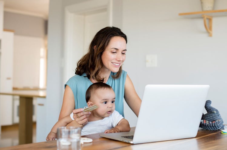 Woman with baby boy online shopping while using laptop computer at home