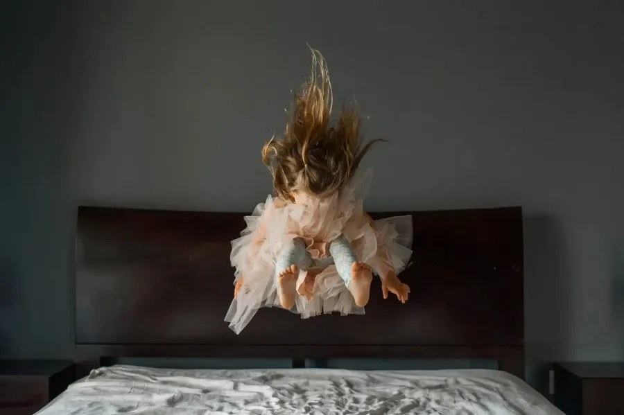 Young girl jumping on the bed in a pink tutu skirt By kimberlywalla