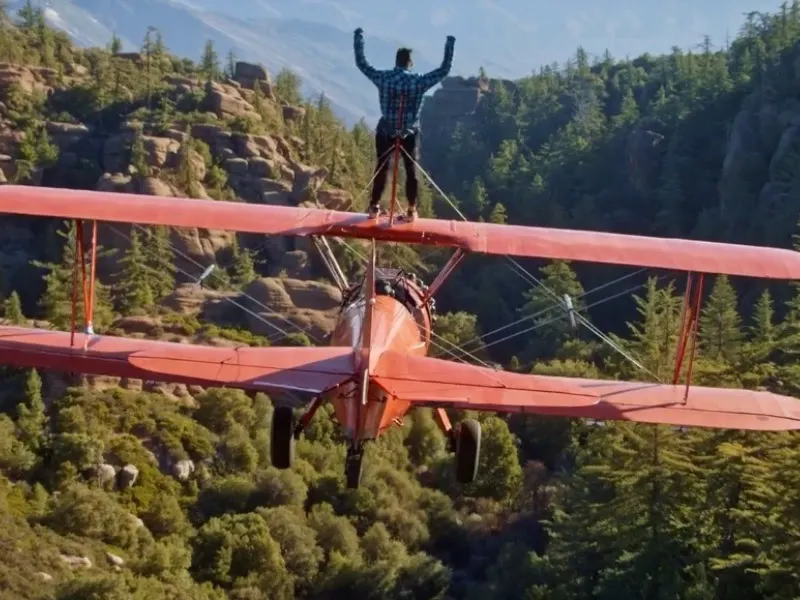 DevinSuperTramp photo of a man standing on top of a red airplane in flight